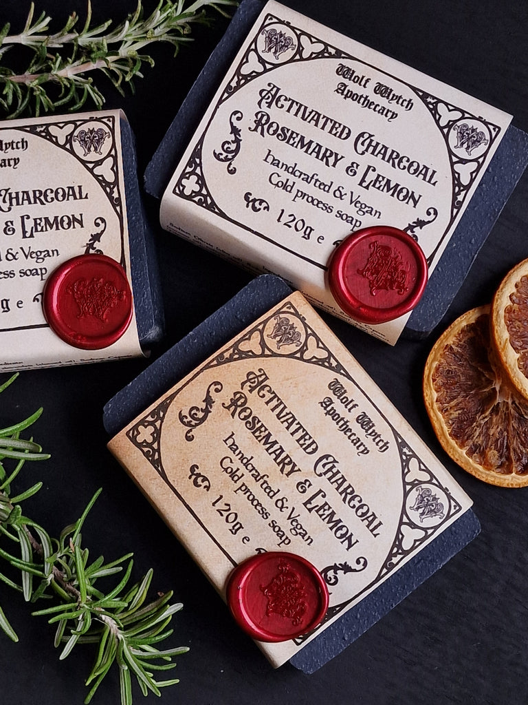 Three bars of soap with decorative labels and red wax seals on a dark surface with herbs.