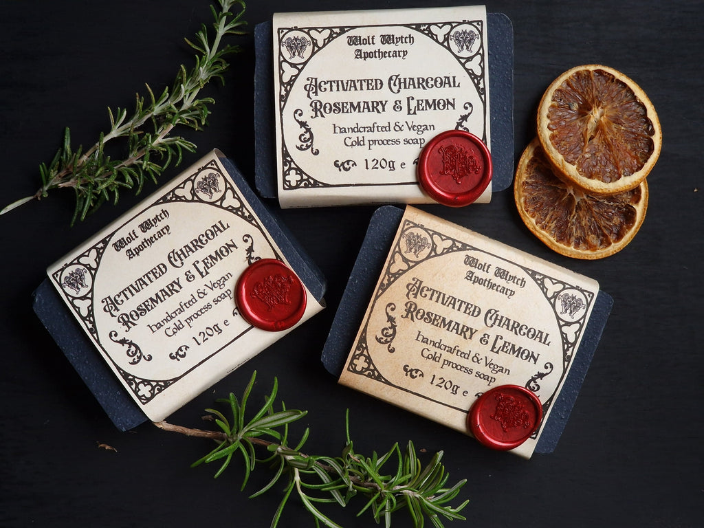 Three bars of soap with decorative labels and red wax seals on a dark surface with herbs and dried oranges.
