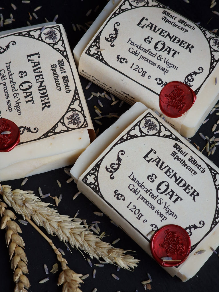 Three bars of lavender and oat soap with decorative labels and red wax seals on a dark background.