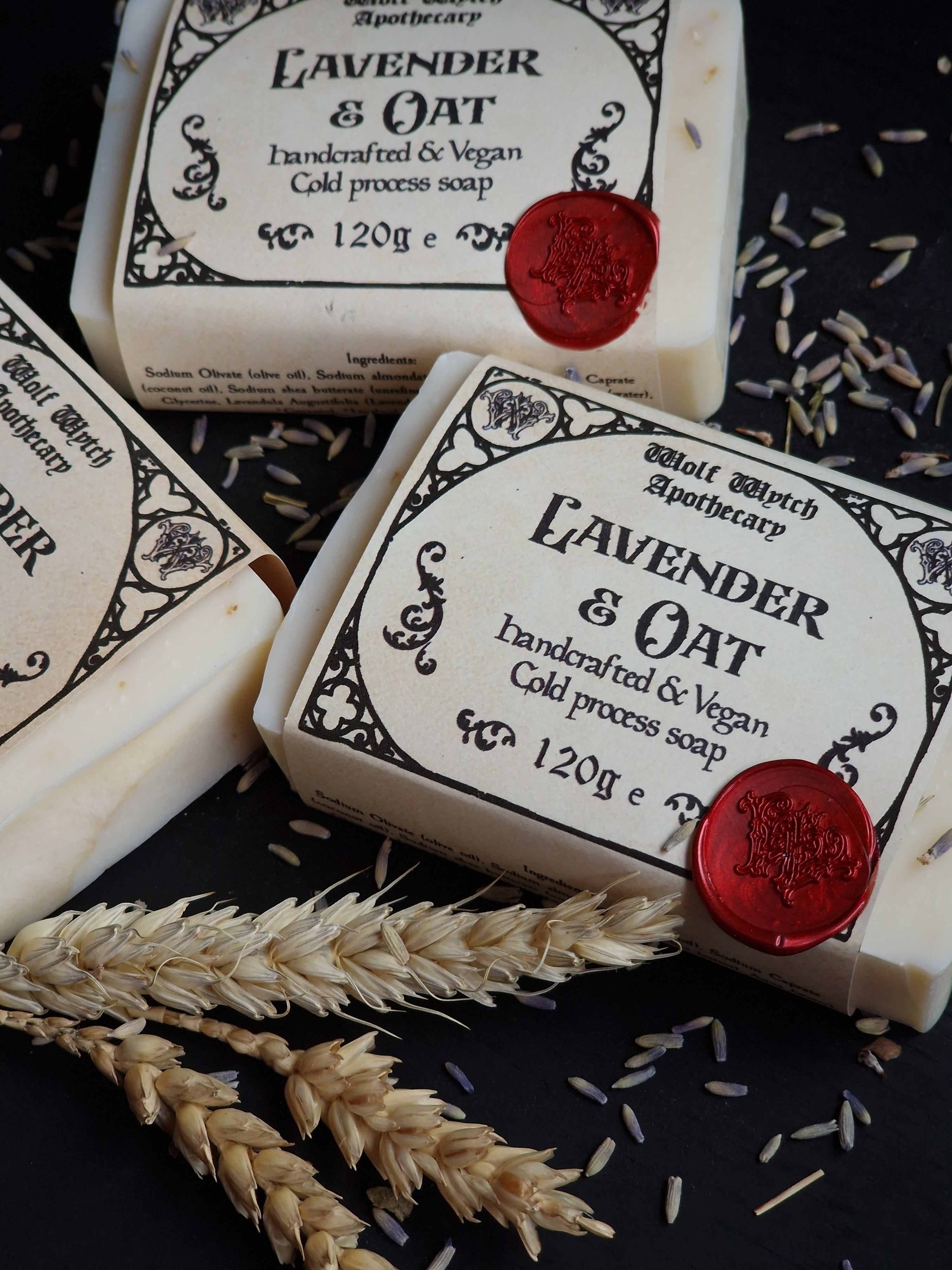 Three bars of lavender and oat soap with red wax seals on a dark background with wheat stalks.
