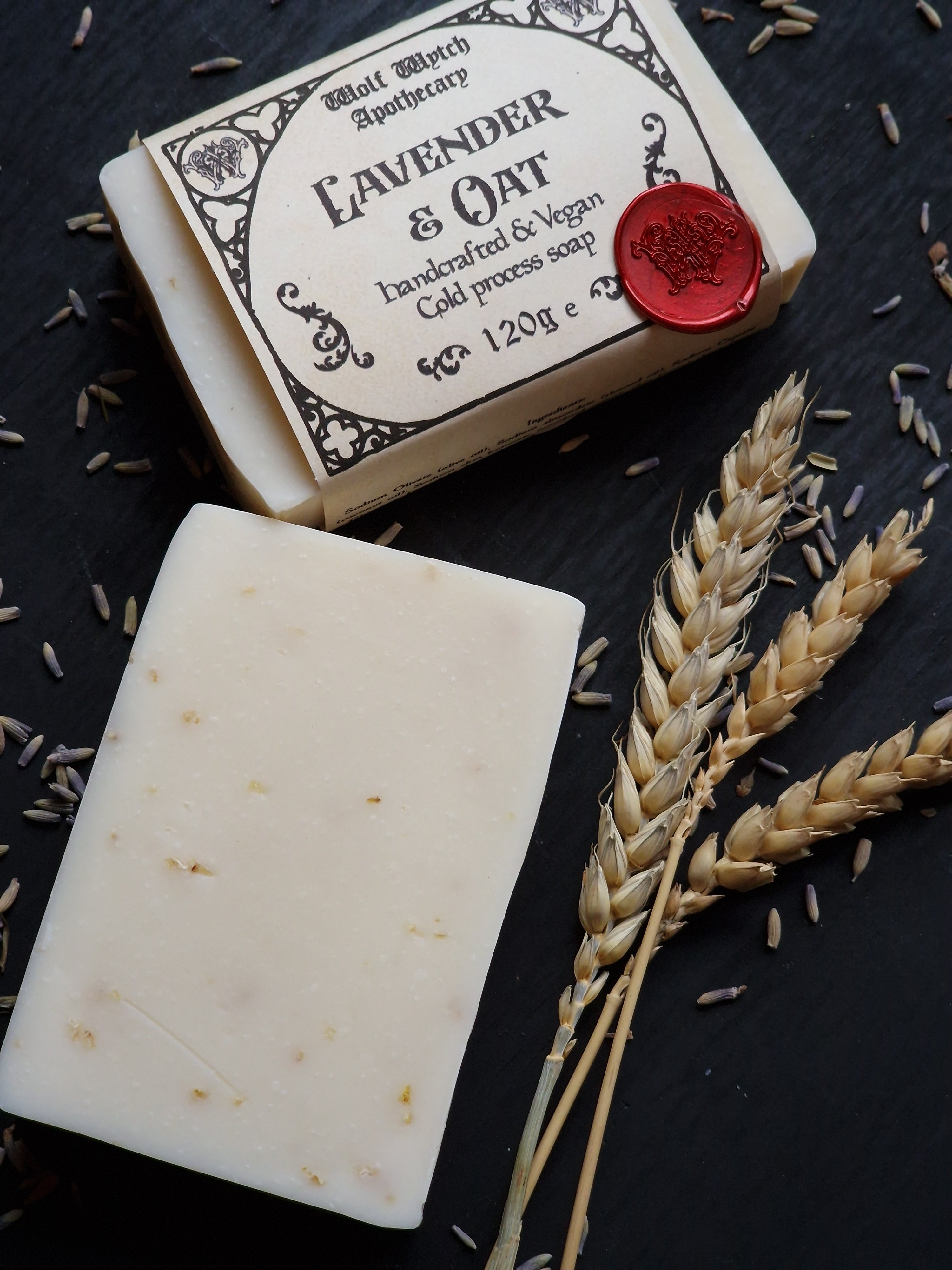 Bar of soap with packaging on a dark surface with lavender flowers