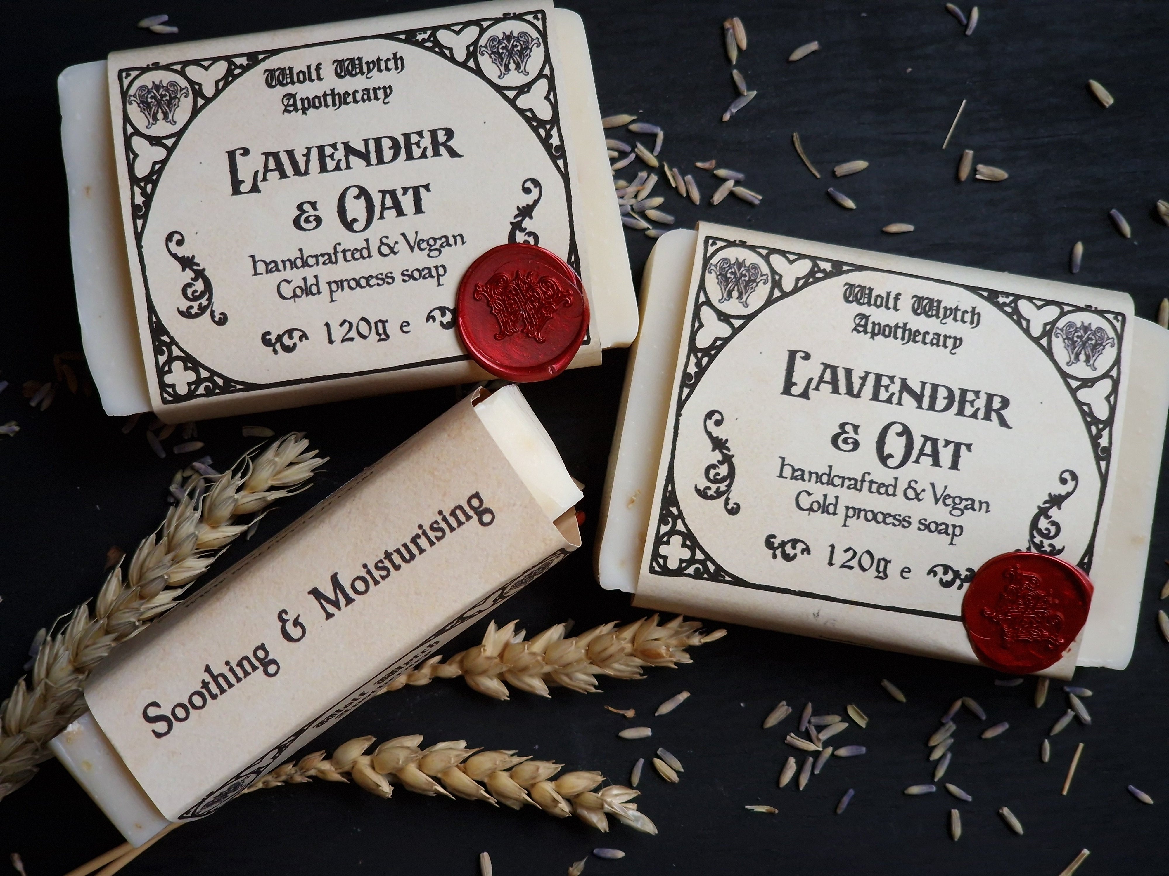 Three bars of soap with labels on a dark surface with lavender flowers.