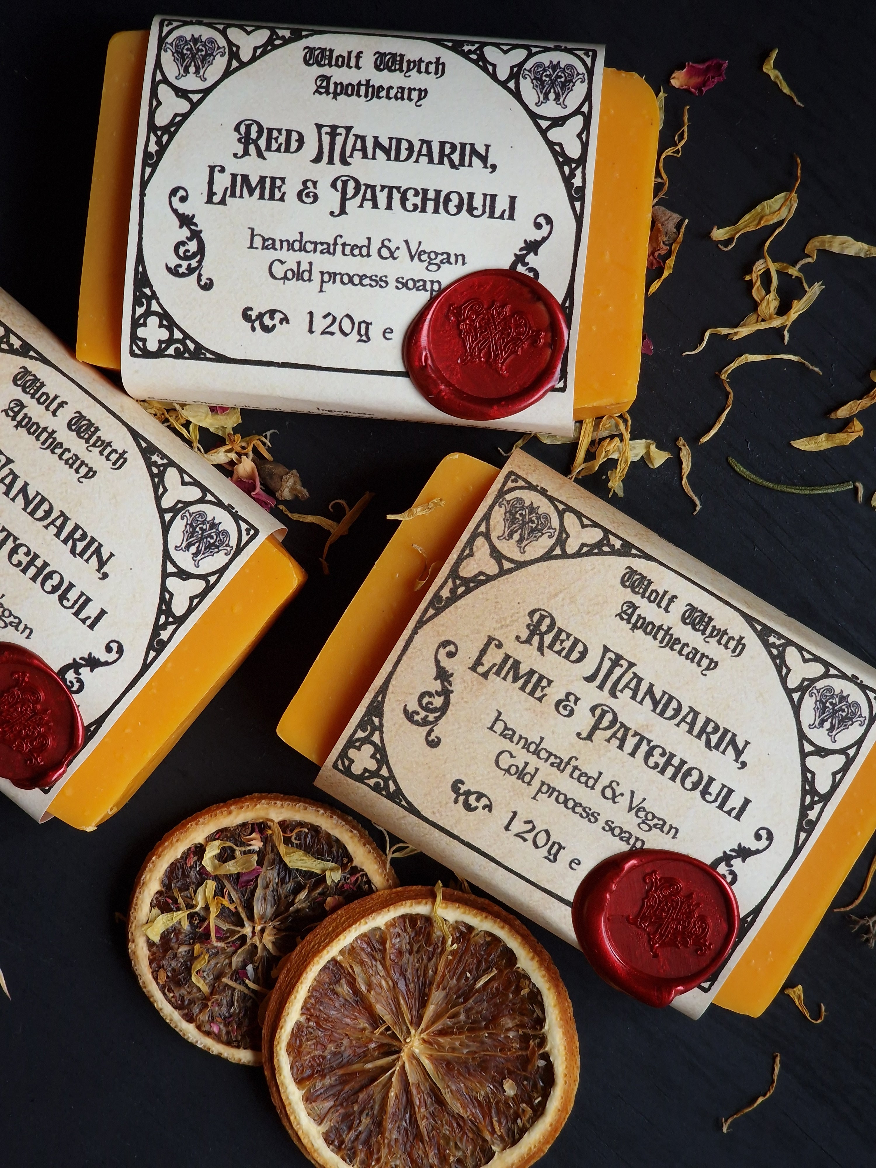 Bar of soap with decorative packaging and red wax seal on a dark surface with dried oranges and leaves.