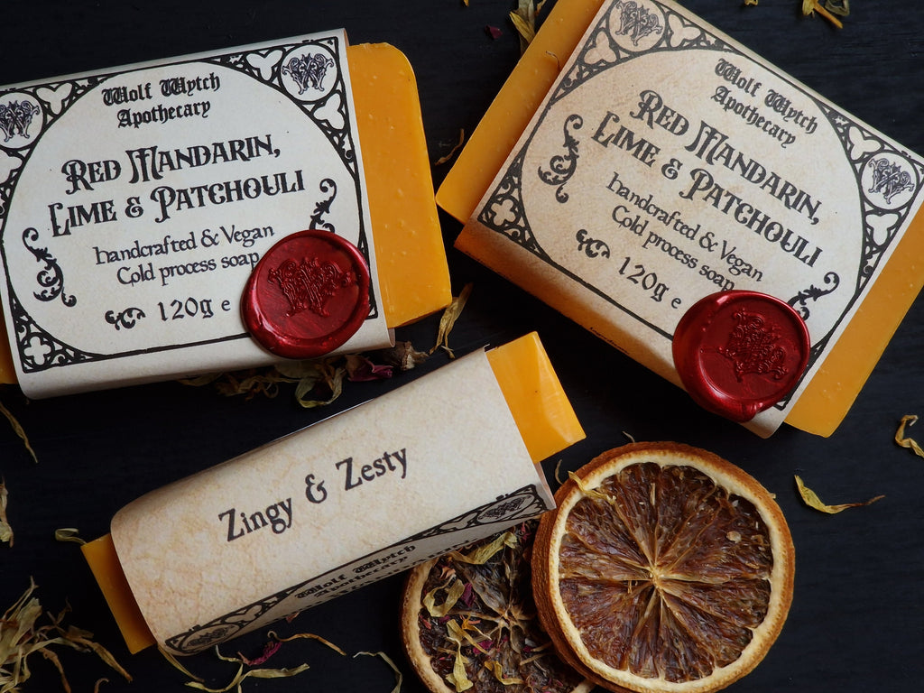 Three soap bars with labels and a dried orange slice on a dark surface