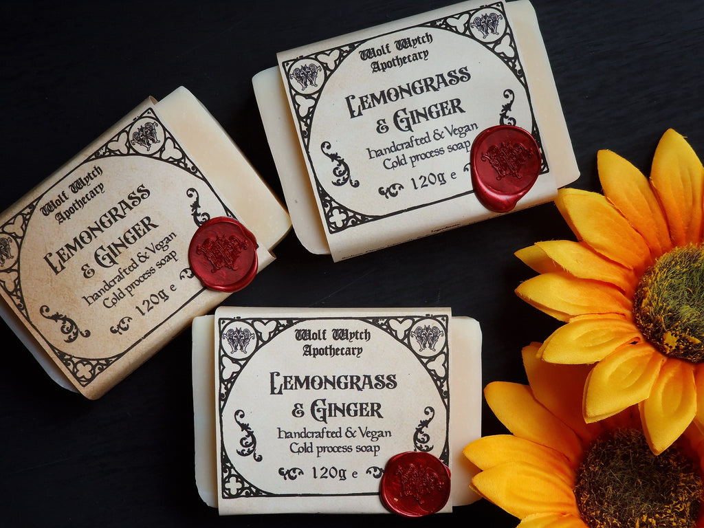 Three bars of Lemongrass & Ginger soap from Wolf Witch Apothecary with a sunflower on a dark background.