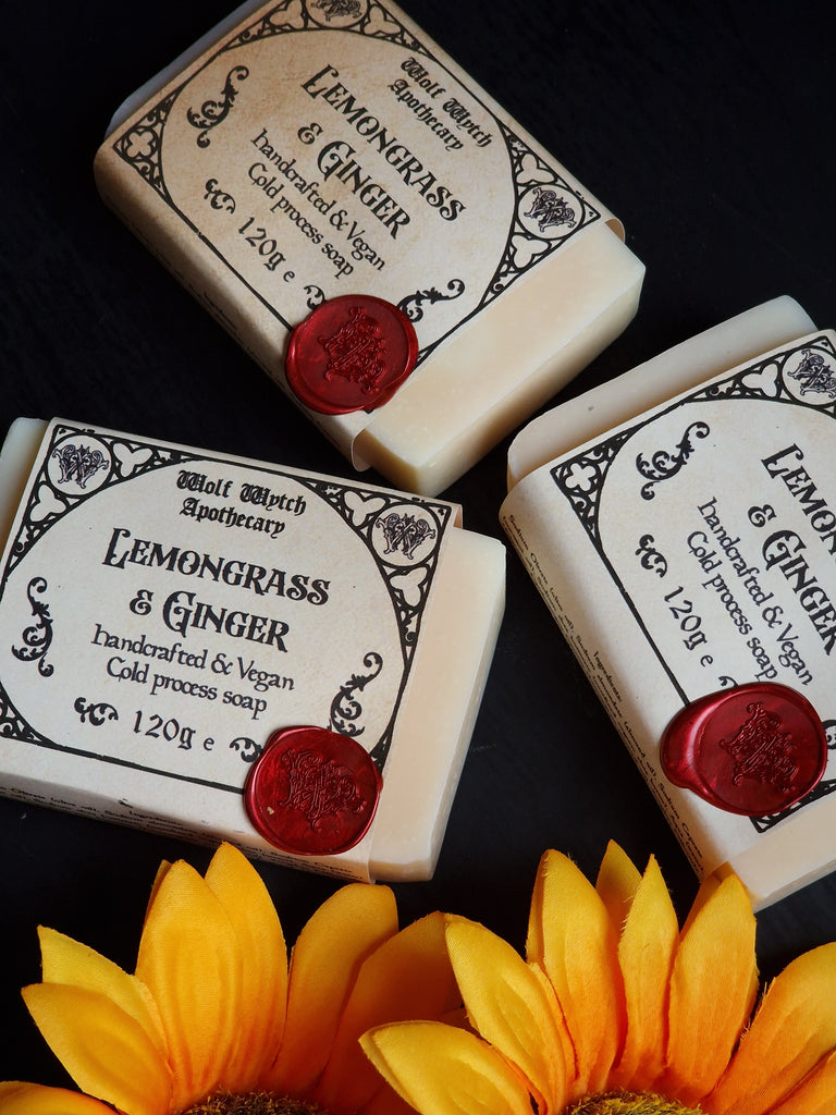Three bars of soap with Lemongrass & Ginger fragrance, surrounded by sunflowers on a dark surface.