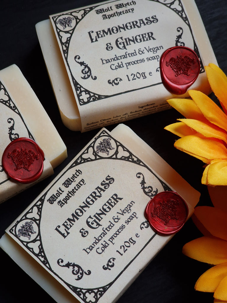 Three bars of soap with decorative labels and red wax seals, accompanied by a yellow flower.