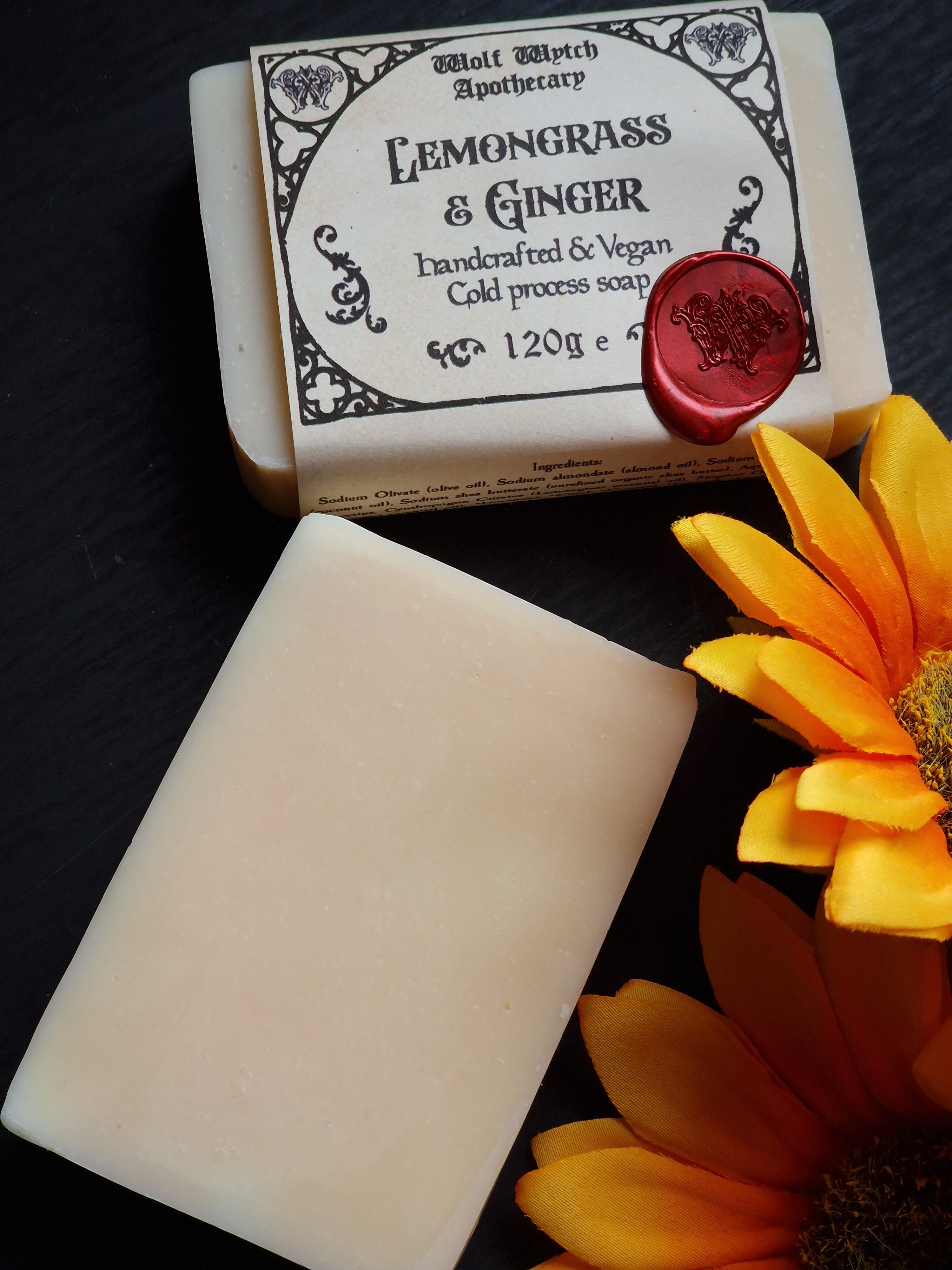 Bar of soap with a decorative label and a yellow flower on a dark surface